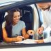 A young woman buys a car in a car showroom. A man signs a car rental agreement.
